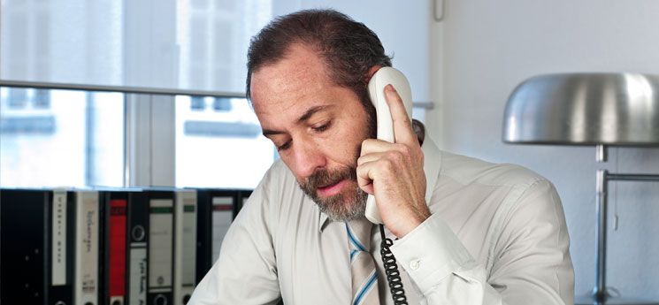 middle aged man with beard talking on landline in office