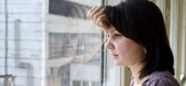 woman in her 30's leaning head against window while looking out