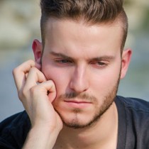 young, sad, pensive man looking down with and resting on face