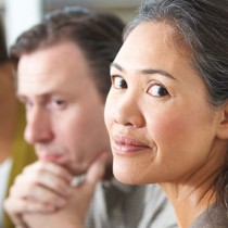 mixed race woman sitting in group session while looking away from group but at camera