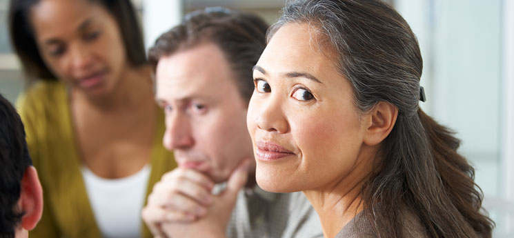 mixed race woman sitting in group session while looking away from group but at camera
