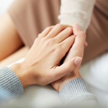 close up of one woman's hands holding another woman's hand to comfort her