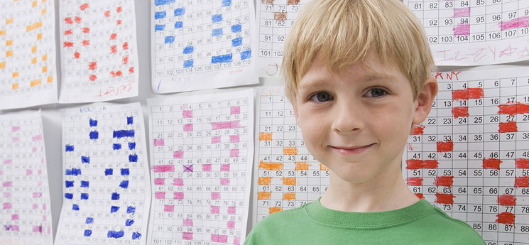 young blonde boy with half smile in elementary school math classroom standing in front of completed worksheets