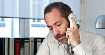 middle aged man with beard talking on landline in office