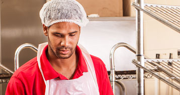 man wearing apron and hair net while working in industrial kitchen