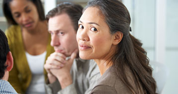 mixed race woman sitting in group session while looking away from group but at camera