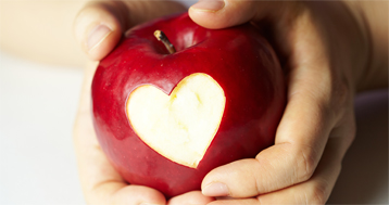 hands holding red apple with heart cut out of it