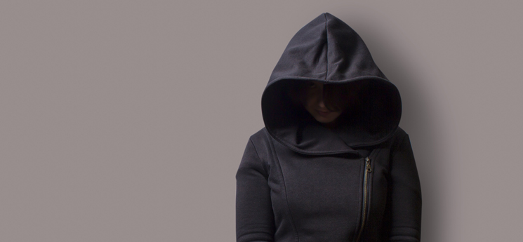 woman in dark, hooded jacket looking down at floor, ashamed